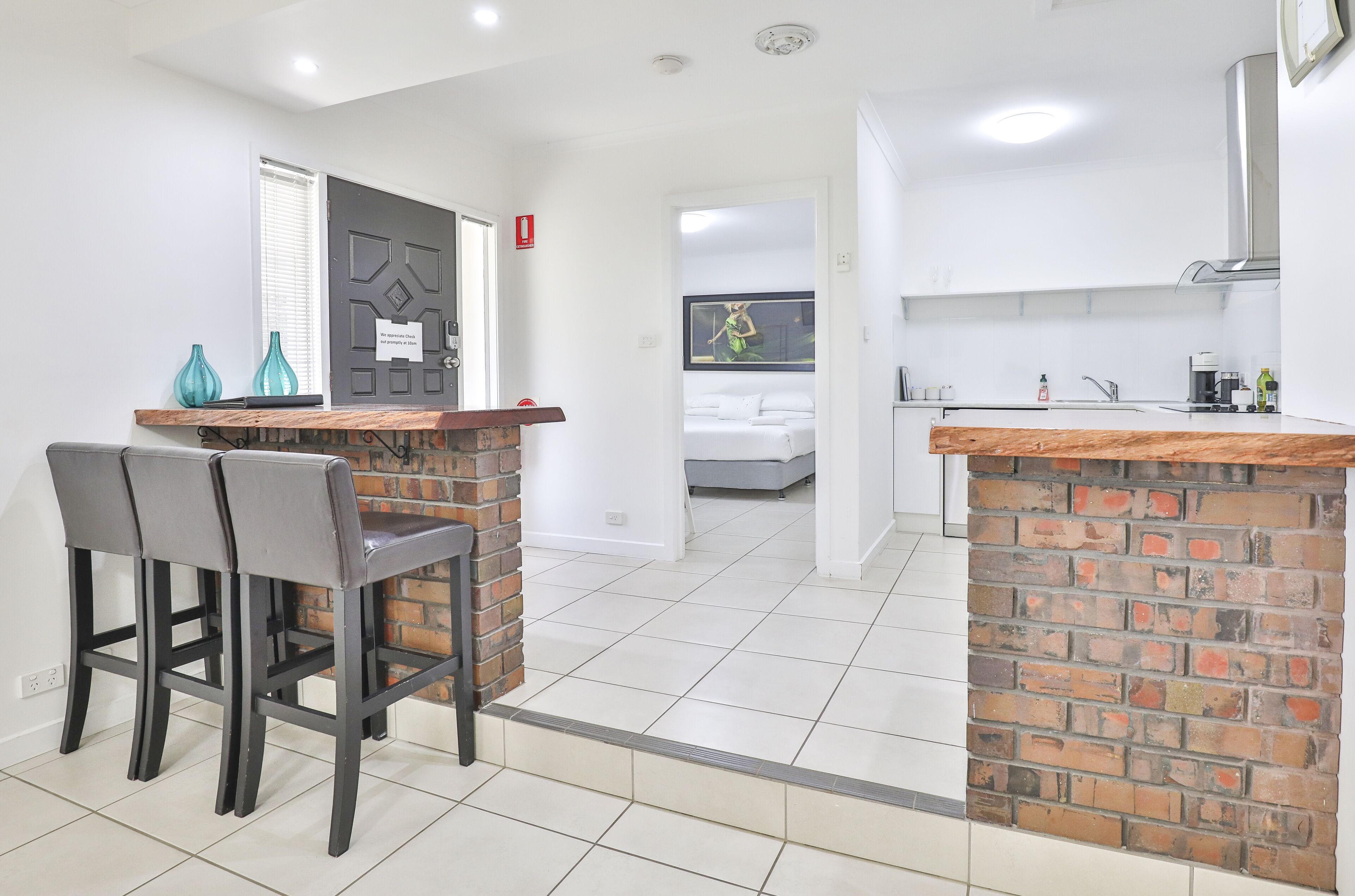 A modern kitchen with white cabinets, a brick accent wall, and a dining area with two chairs and a wooden table.