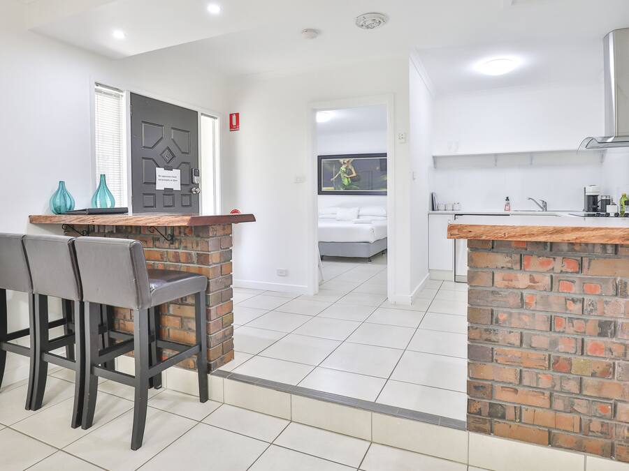 A modern kitchen with white cabinets, a brick accent wall, and a dining area with two chairs and a wooden table.