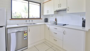 Cozinha moderna com armários brancos, máquina de lavar louça, janela e bancada com chaleira e cafeteira.