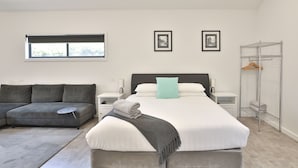 Quarto moderno com uma cama grande, um sofá cinzento, um closet espaçoso e uma janela com persianas.