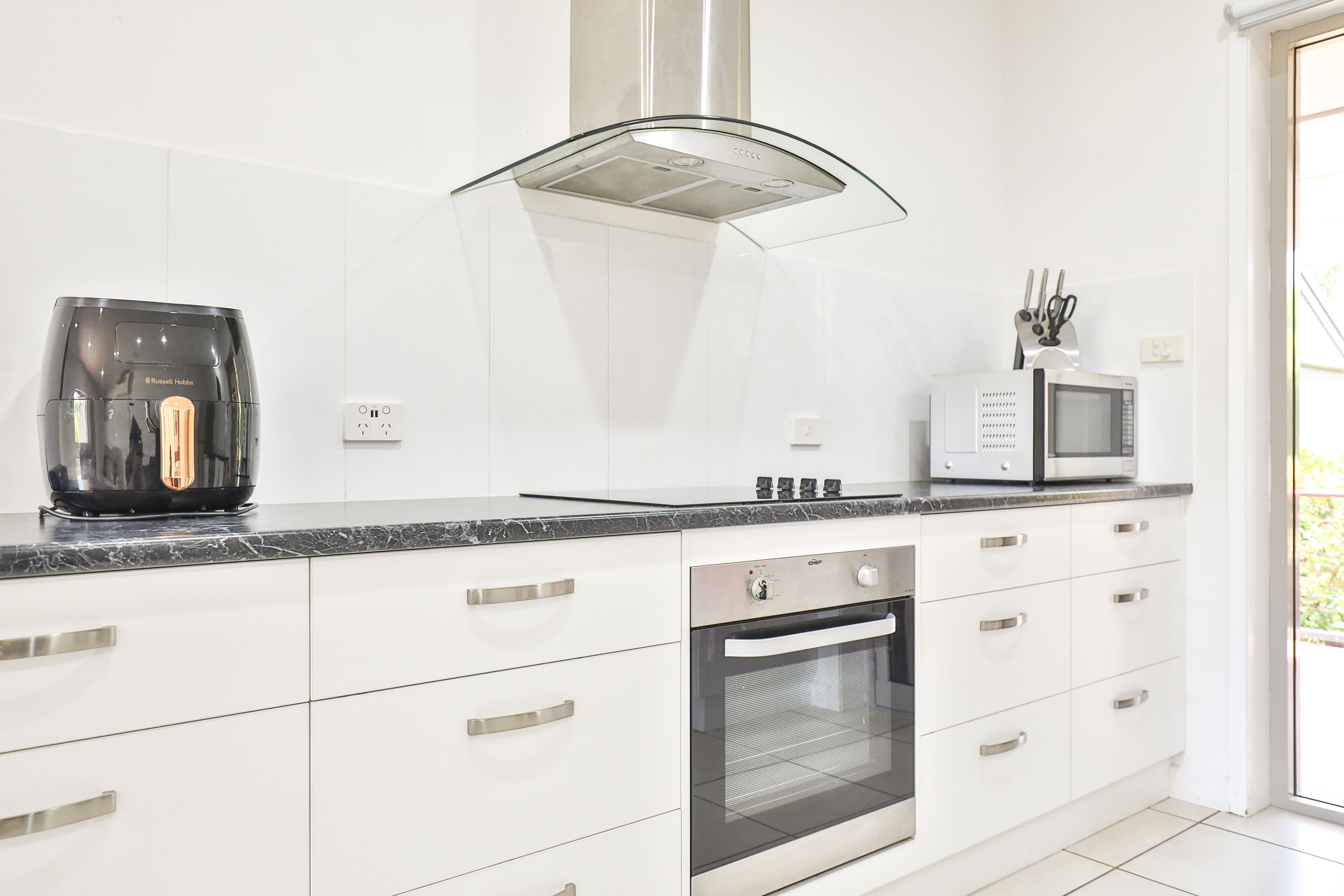 A modern kitchen with white cabinetry, a built-in oven, a coffee maker, and a microwave.