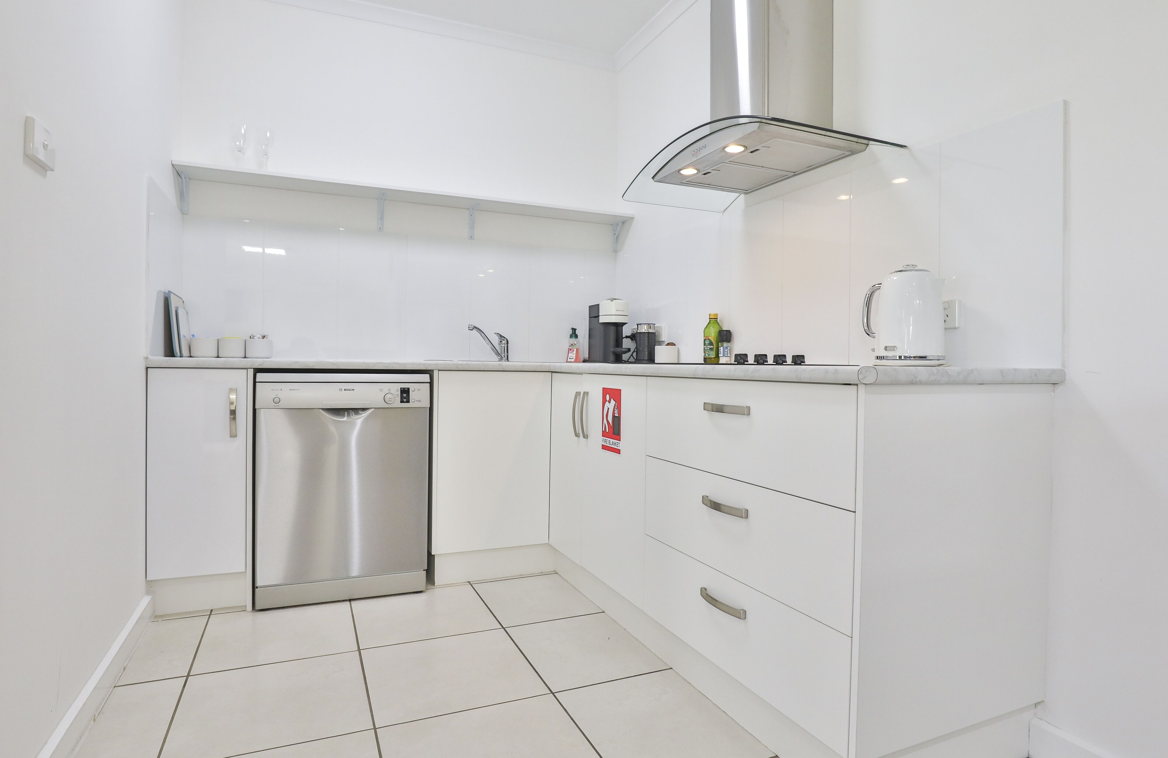Una cocina moderna con armarios blancos, lavavajillas de acero inoxidable, cafetera y hervidor.