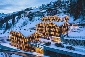 A hotel with a modern architectural design, featuring multiple balconies and a ski slope in the background. - GLEMM by AvenidA Superior Hotel & Residences (Saalbach-Hinterglemm)