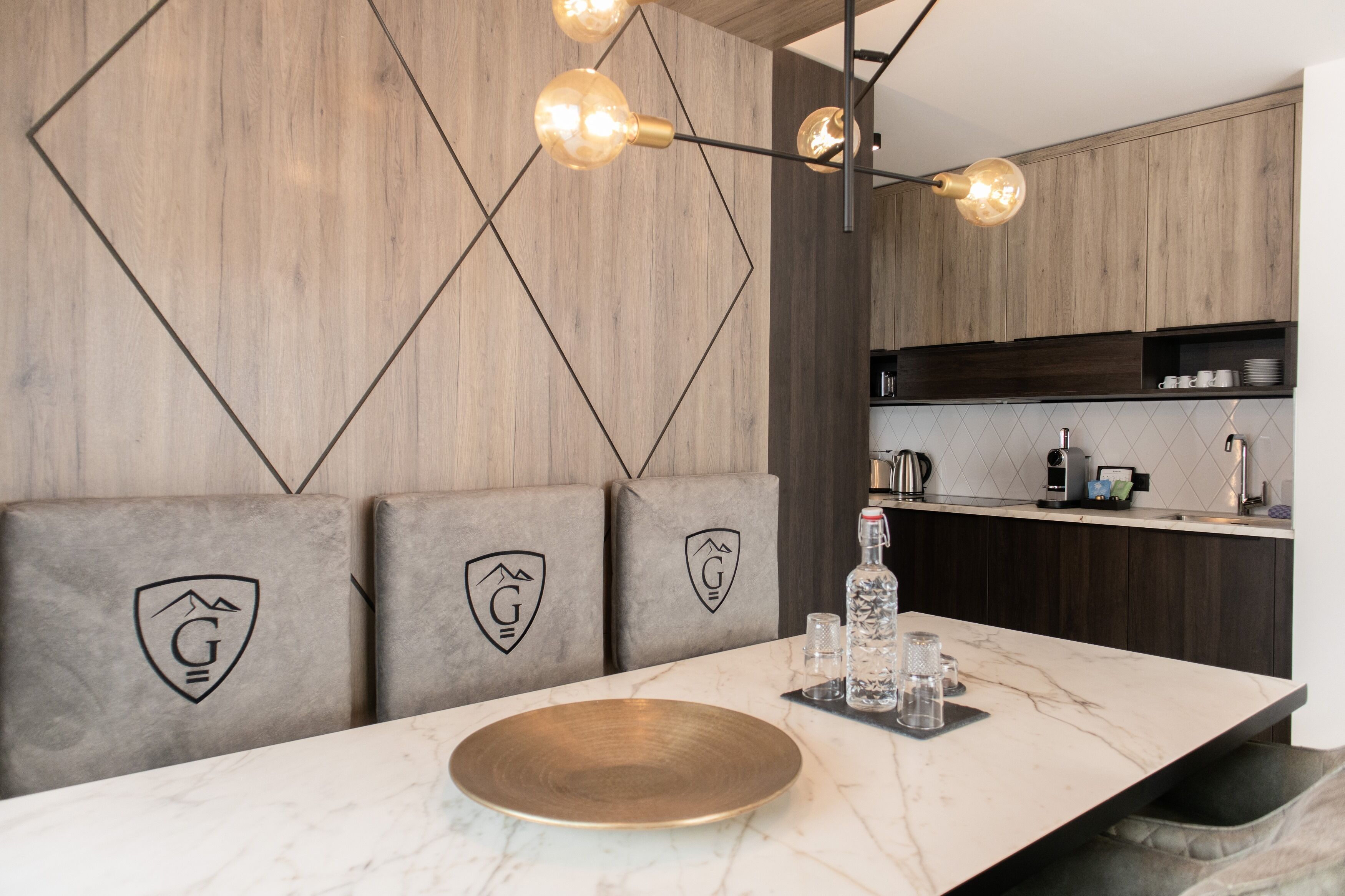 Una cocina moderna con encimera de mármol, paneles de madera y una zona de estar con bancos acolchados.