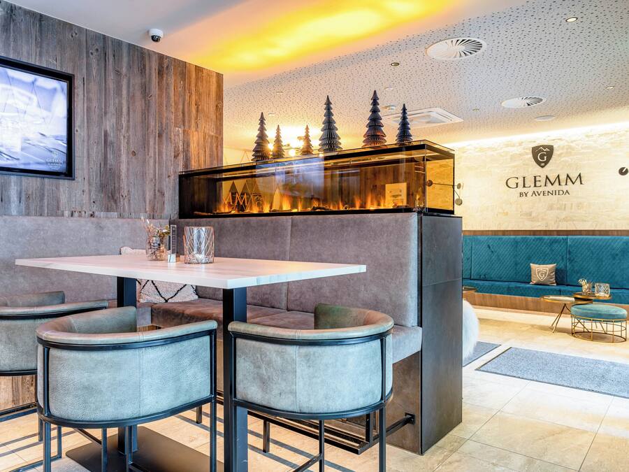 A modern interior with a dining area featuring a round table and four chairs, a sofa, and a wall-mounted display.