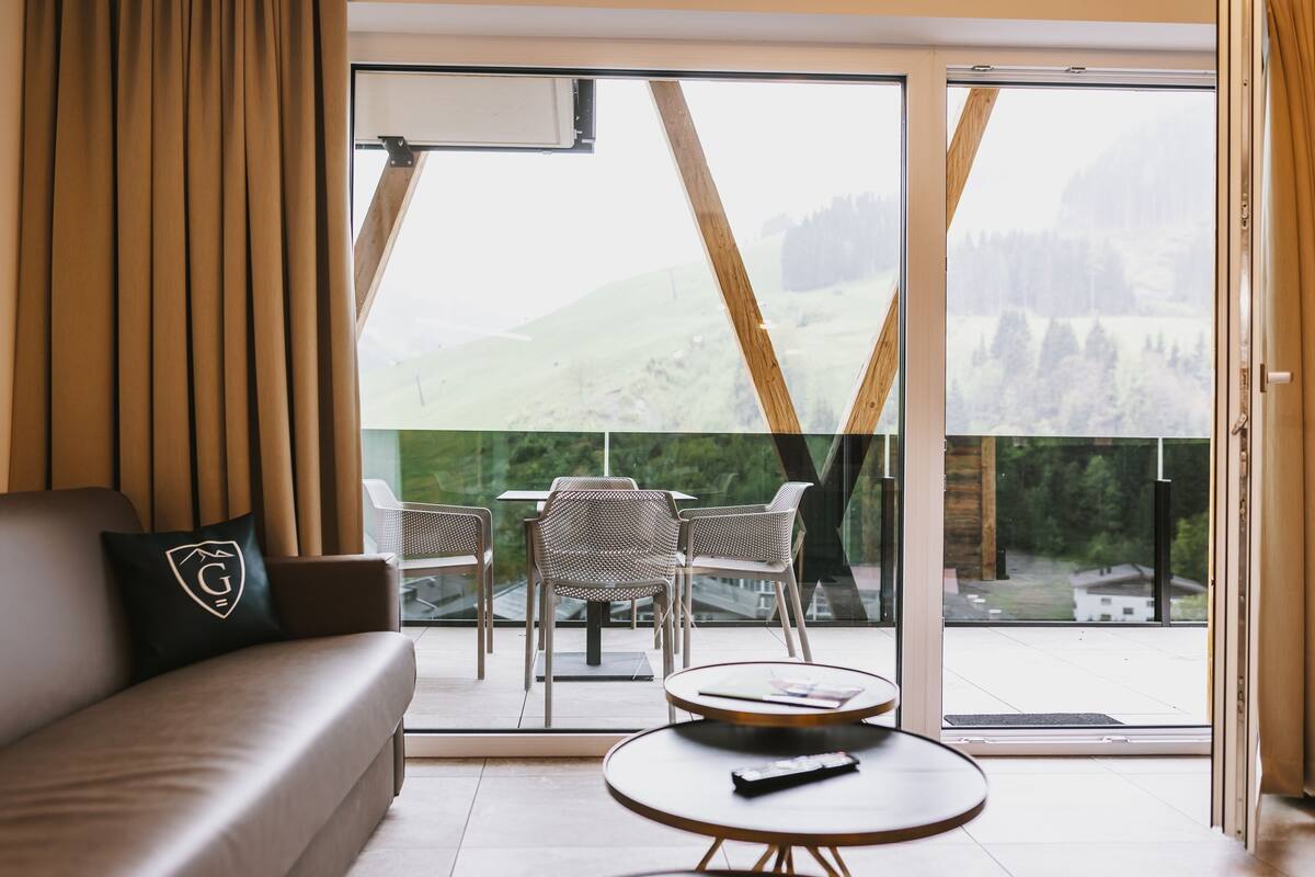 Ein modernes Hotelzimmer mit einer Couch, einem runden Tisch und einem Balkon mit Stühlen und Tisch.