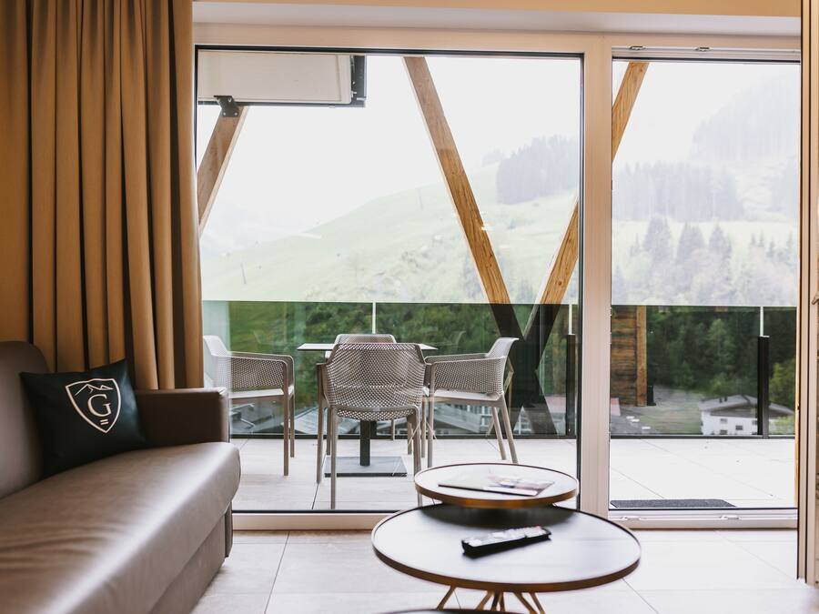 Een moderne hotelkamer met een bank, een ronde tafel en een balkon met stoelen en een tafel.