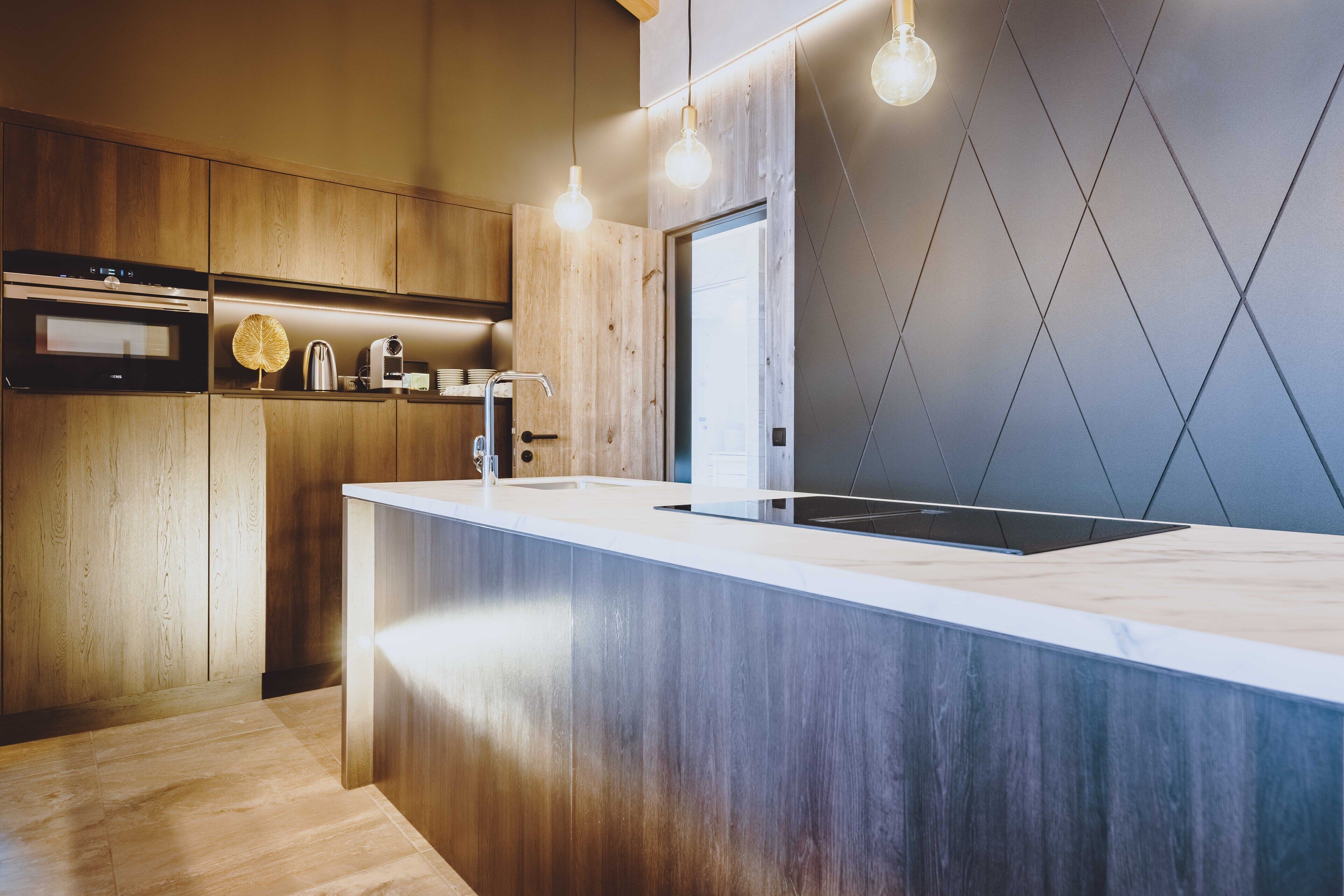A modern kitchen with wooden cabinetry, a marble countertop, and pendant lighting.