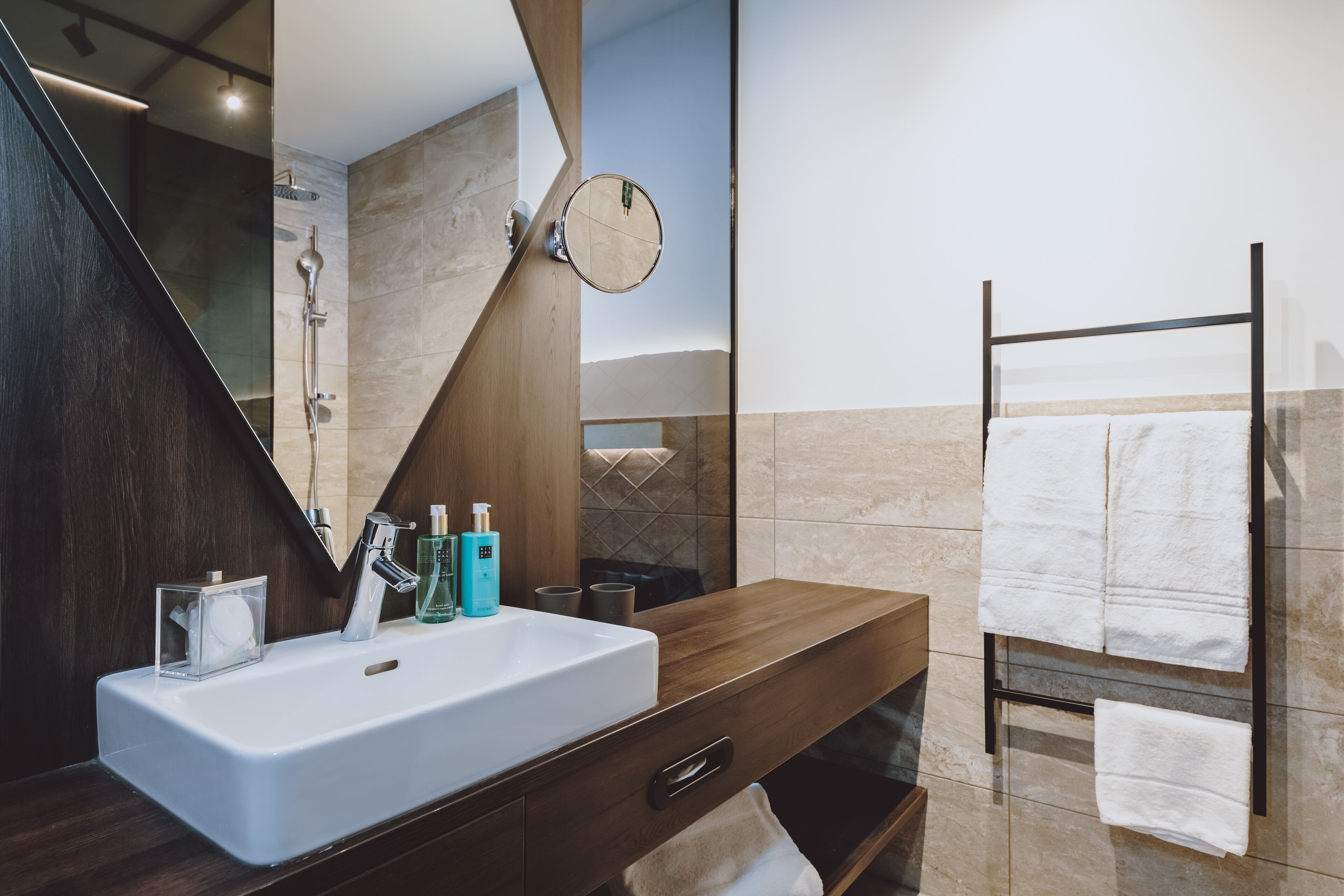 Een moderne badkamer met een grote spiegel, een witte wasbak en een handdoekrek.