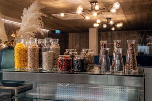 A display of various spices and grains in clear glass bottles on a shelf. - GLEMM by AvenidA Superior Hotel & Residences (Saalbach-Hinterglemm)