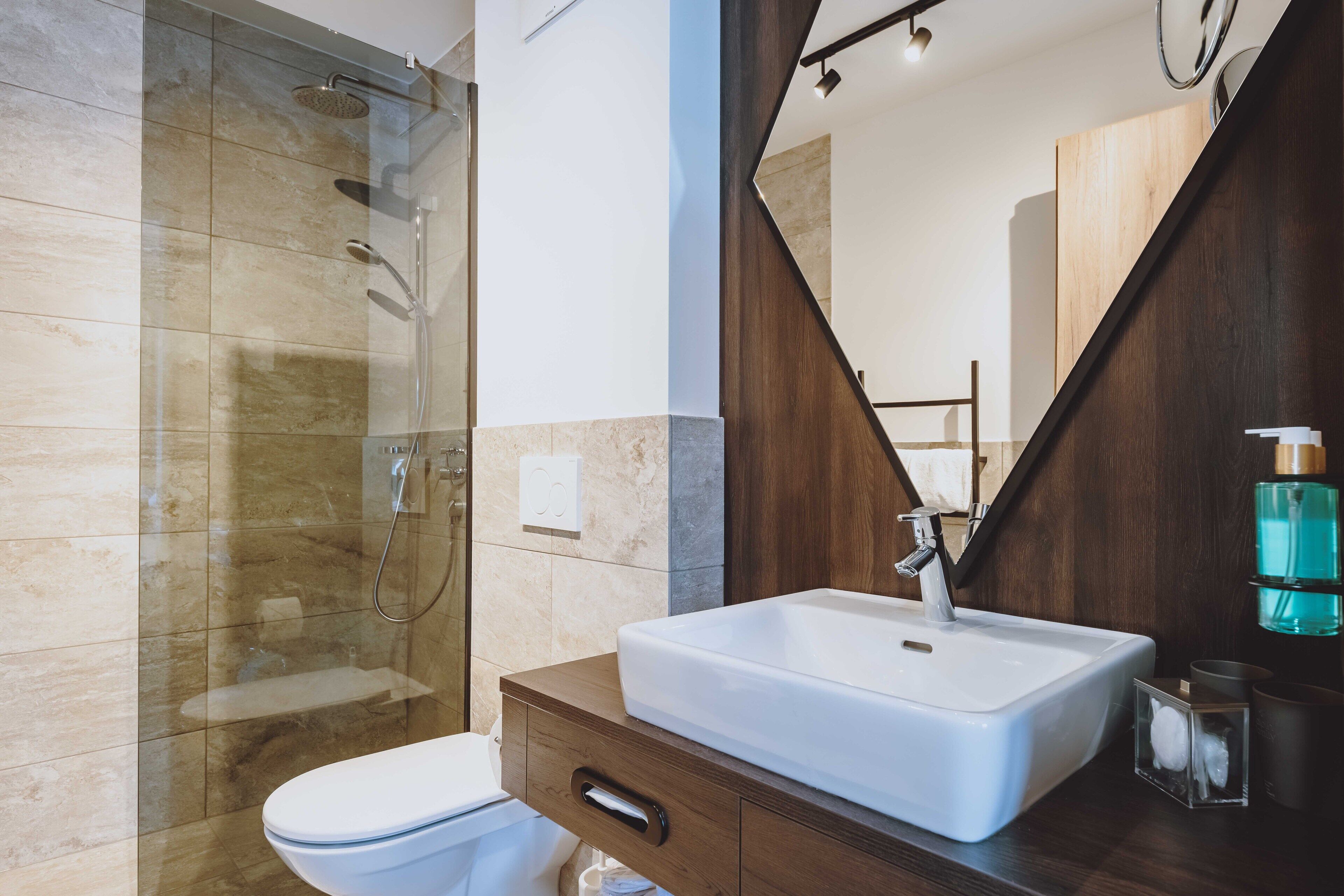 A modern bathroom with a glass shower enclosure, a white sink, and a wooden vanity.