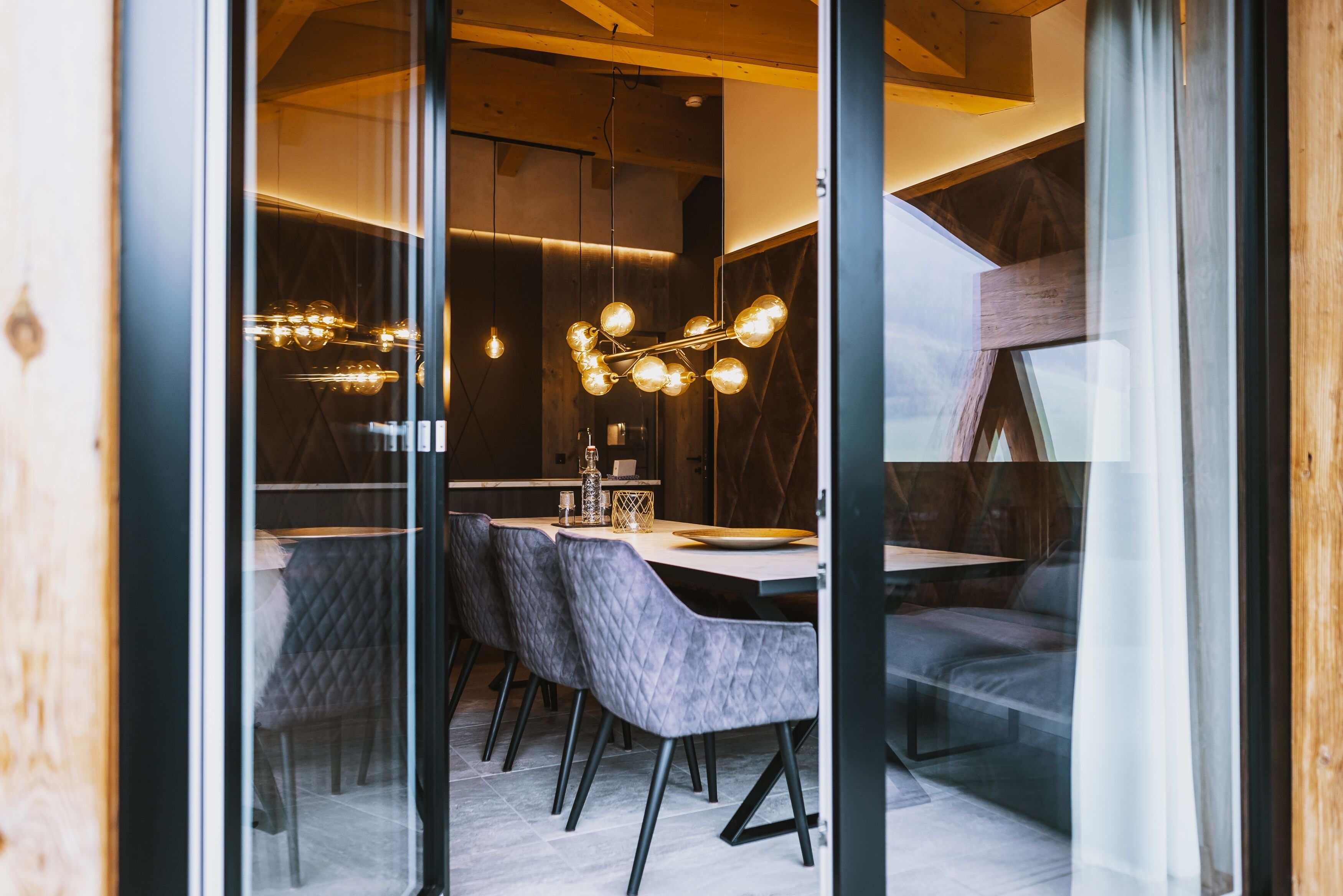 Un espace repas moderne avec une cloison en verre, un plafond en bois et un lustre.