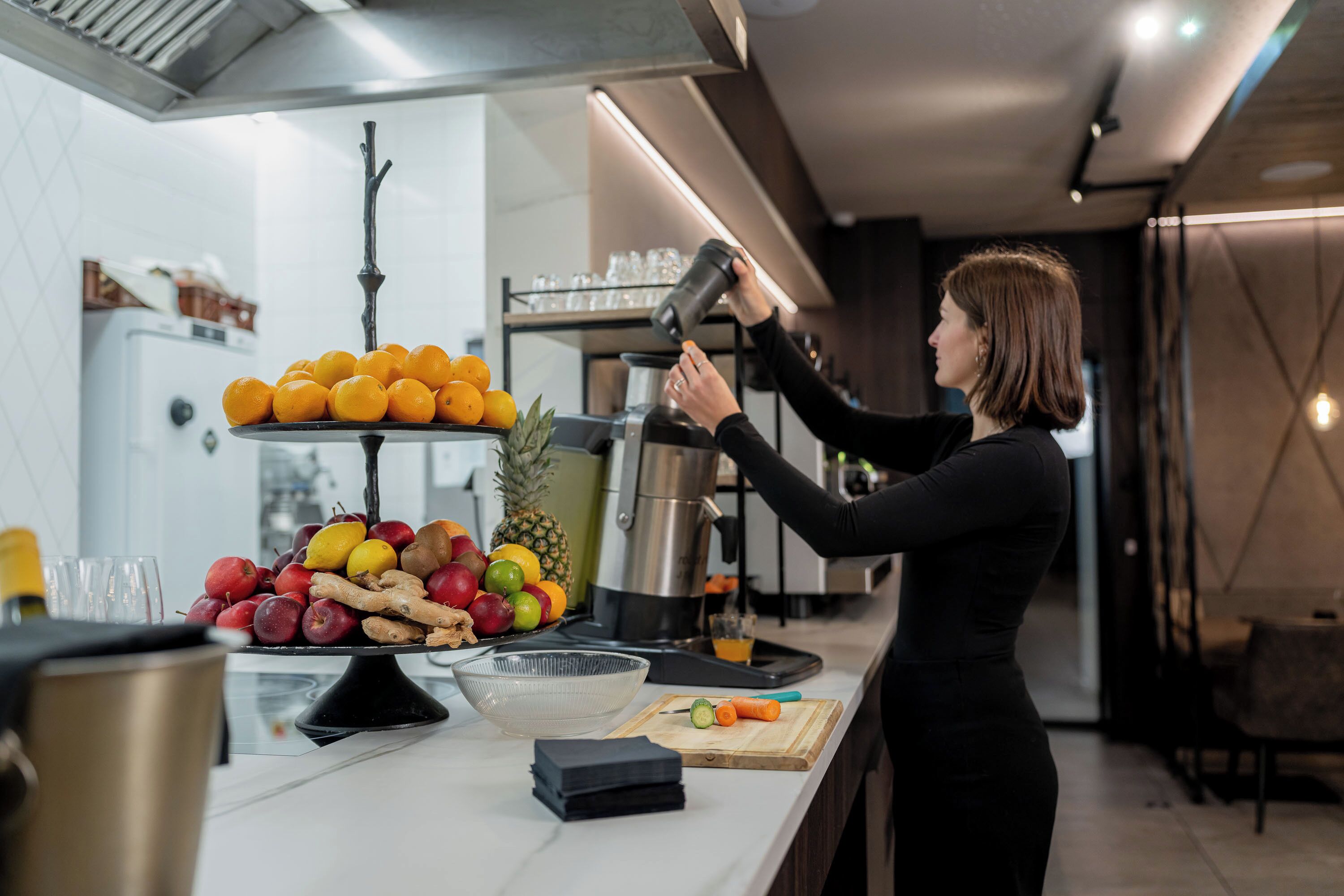 A modern kitchen with a fruit display, a coffee machine, and a person preparing a drink.