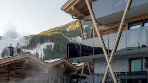 A modern building with a pool, wooden deck, and mountain views. - GLEMM by AvenidA Superior Hotel & Residences (Saalbach-Hinterglemm)