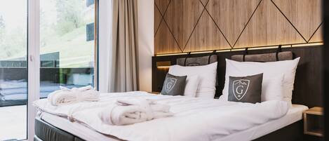Una cama bien hecha con toallas, un cabecero de madera y vistas al exterior a través de una puerta corredera.