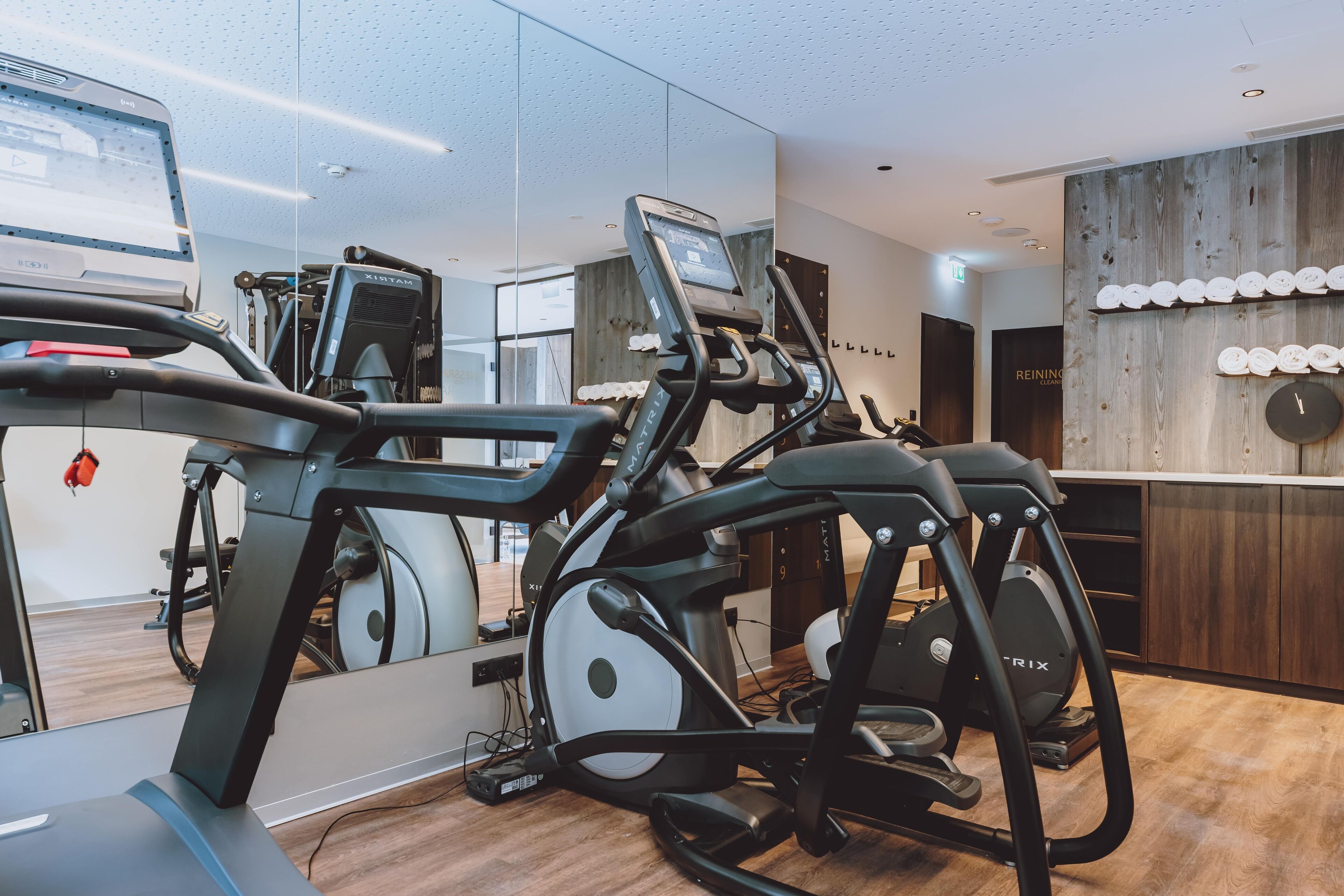 Un gimnasio con equipo de ejercicio, un espejo y una pared de madera con un reloj.