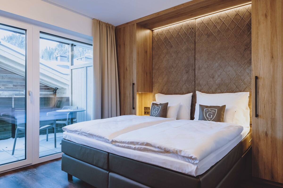 Ein modernes Schlafzimmer mit einem großen Bett, einem Holz-Kopfteil und einer Schiebeglastür zu einem Außenbereich.