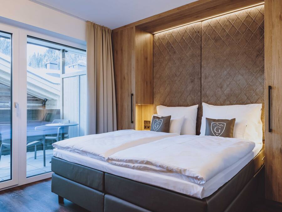 Un dormitorio moderno con una cama grande, cabecera de madera y puerta corrediza de vidrio que da a un espacio exterior.