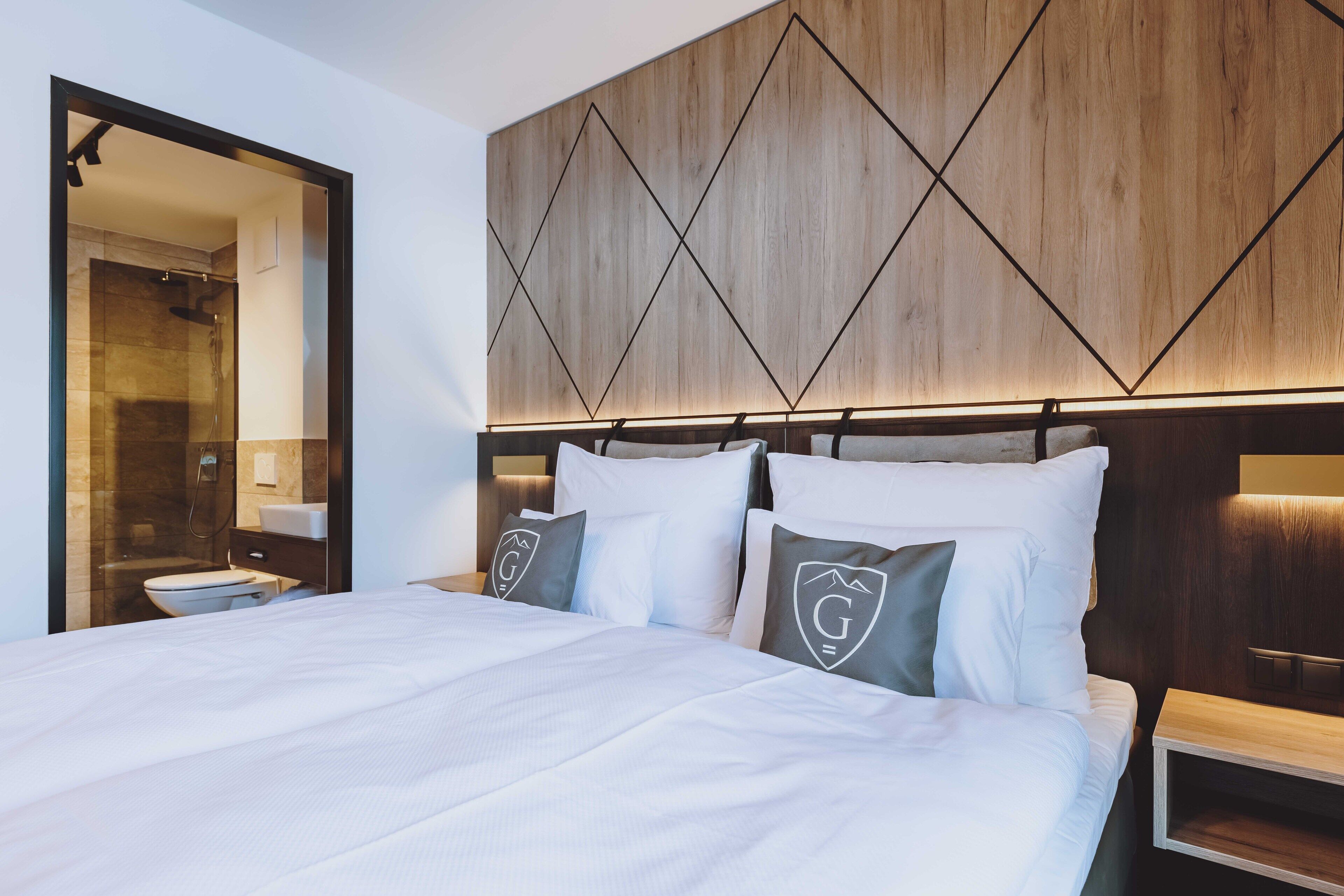 Een moderne hotelkamer met een groot bed, een houten hoofdeinde en een douche die zichtbaar is door een open deur.