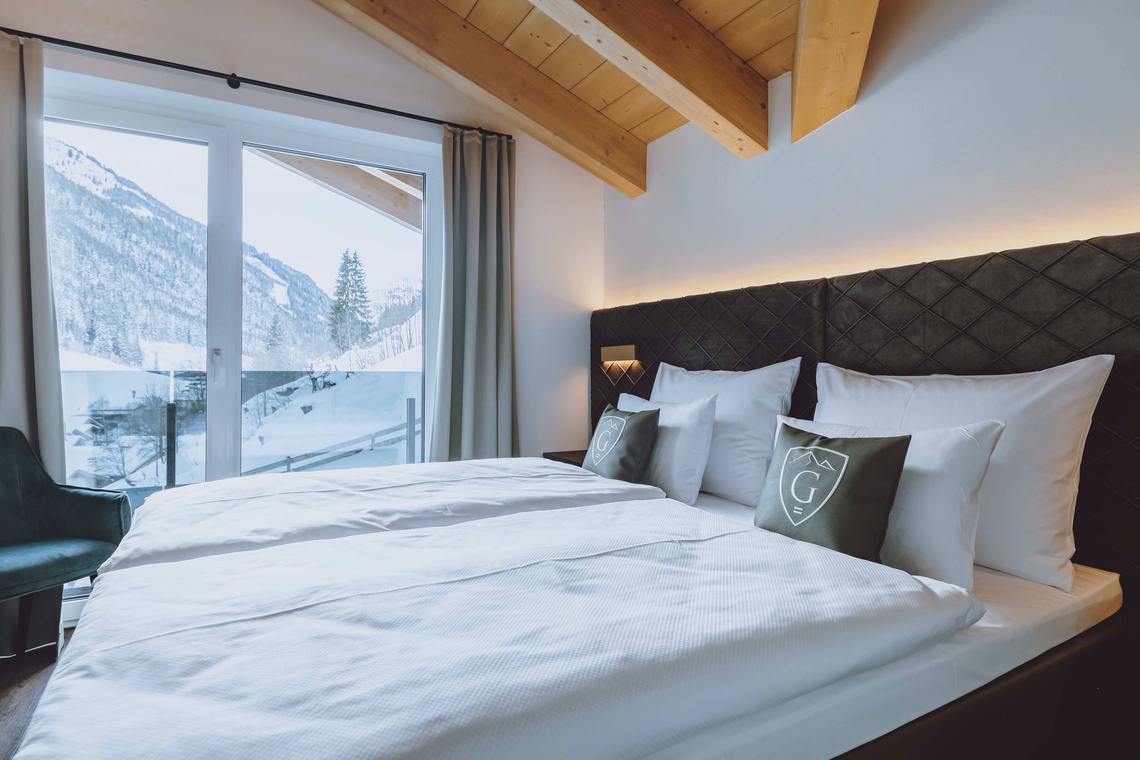 Une chambre d’hôtel avec un grand lit, une vue sur des montagnes enneigées et un plafond en bois.