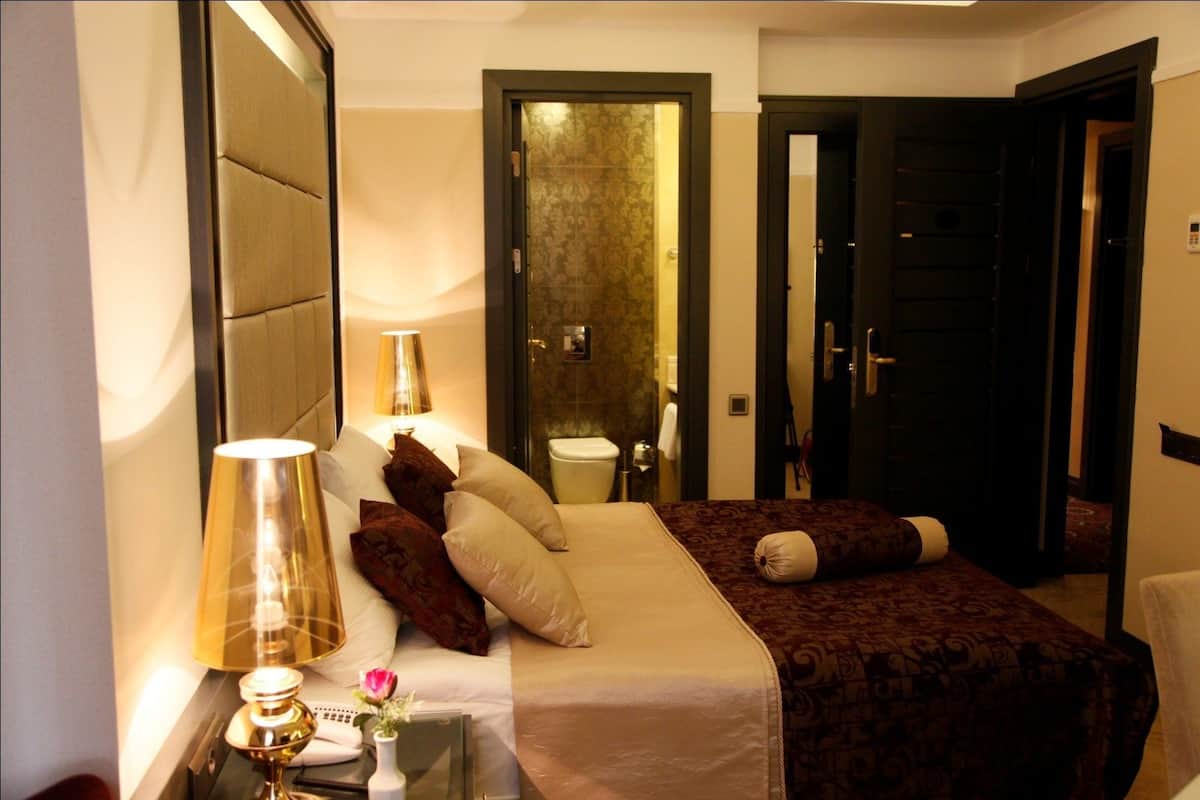 Quarto de hotel com cama, mesa de cabeceira, abajur e espelho.