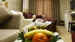 A hotel room with a modern design, featuring a sofa, a dining table with fruit, a desk, and a large window with curtains. - Mirilayon Hotel (Istanbul)