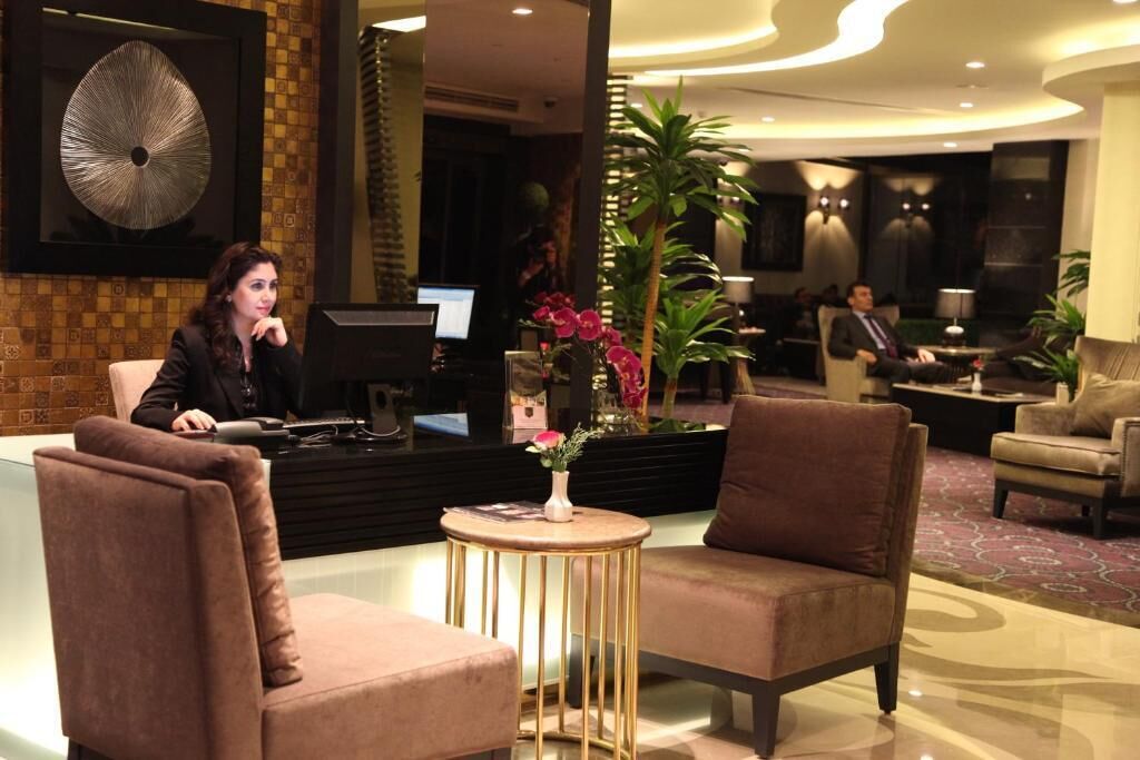 A lobby with a reception desk, two armchairs, a round table with a vase of flowers, and a large abstract painting on the wall.