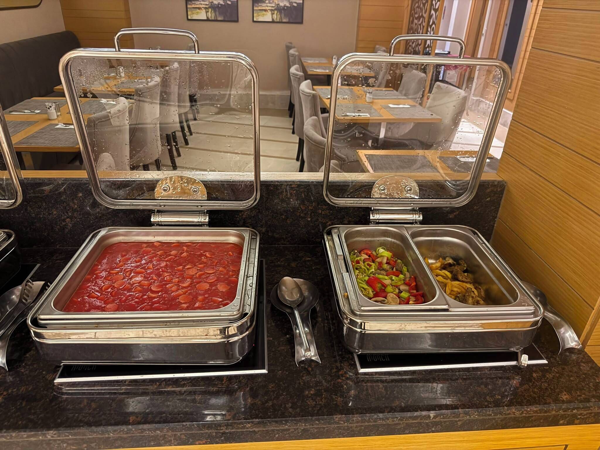 Mostrador de buffet con diversas opciones de comida, incluyendo un plato de judías rojas, verduras mezcladas y champiñones a la parrilla.