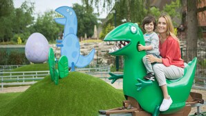 A child and an adult on a green dinosaur-shaped ride at an amusement park. - Heide Park Holiday Camp (Soltau)
