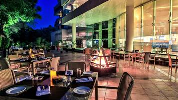 An outdoor dining area with tables and chairs, a fire pit, and a view of the building's interior.