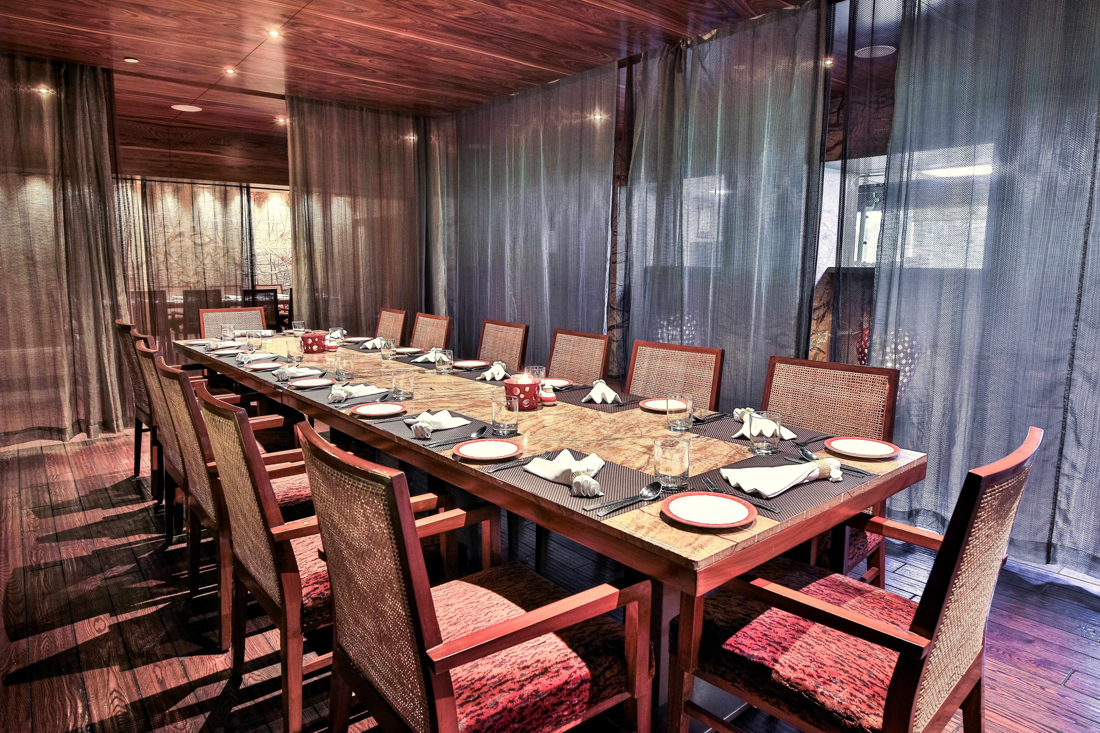 A conference room with a long table set for a meeting, surrounded by chairs with red cushions.