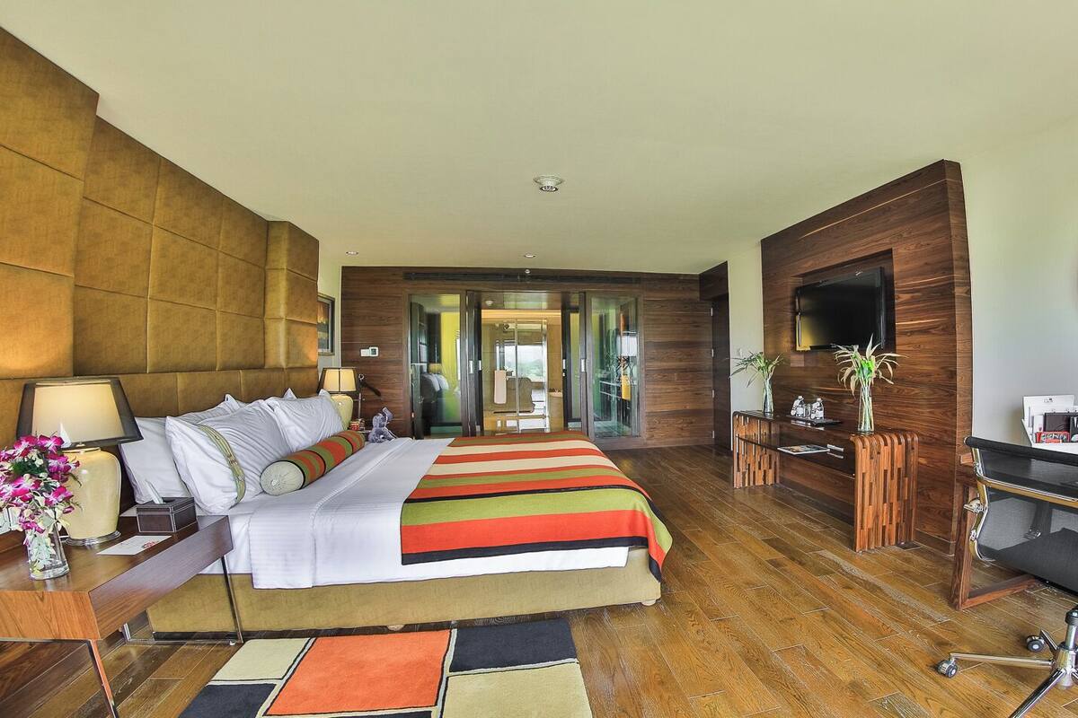 A hotel room with a large bed, a desk with a chair, a TV, and a mirror.