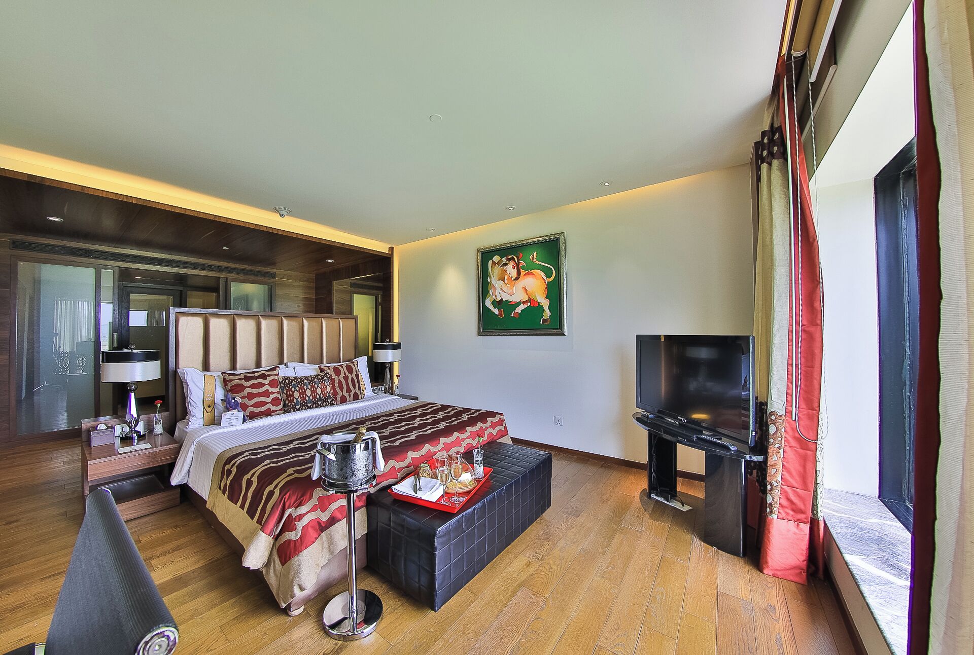 A hotel room with a bed, a TV, a painting, and a window with curtains.