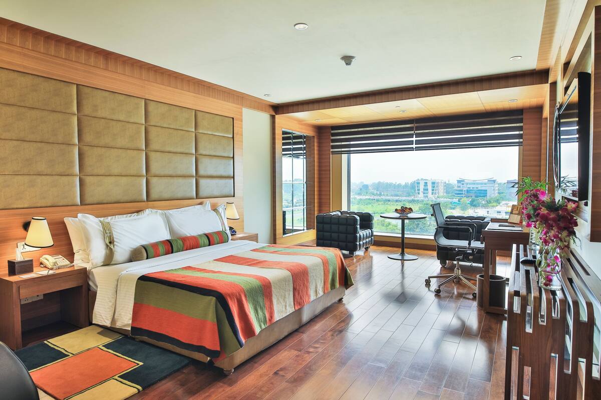 A modern hotel room with a large bed, a desk, and a view of the city.