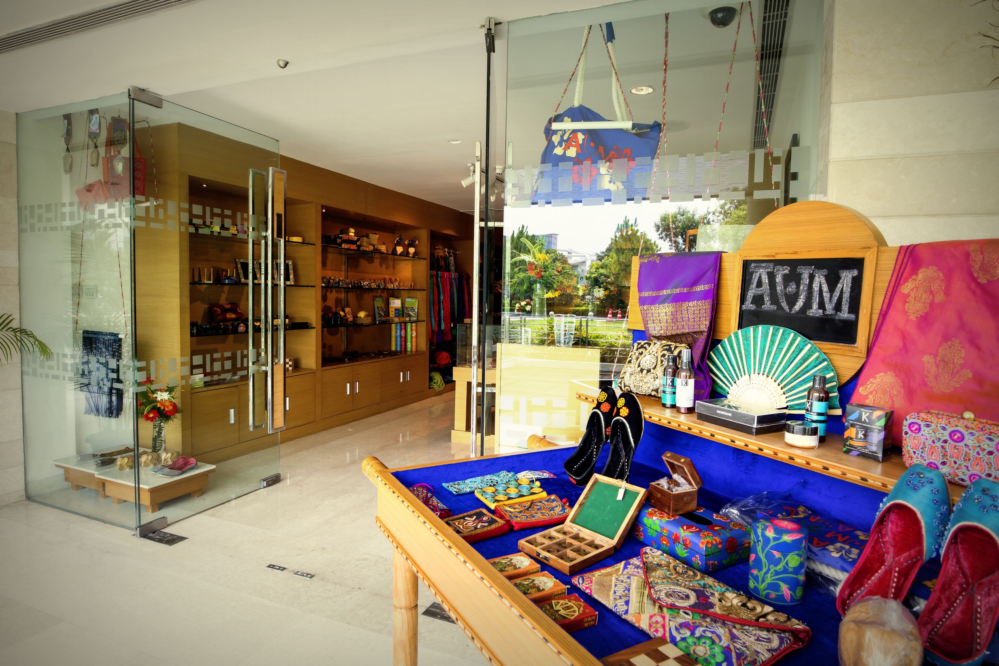 Hall de un hotel boutique con un panel de vidrio, un mostrador de recepción de madera y una variedad de textiles y accesorios de colores exhibidos.