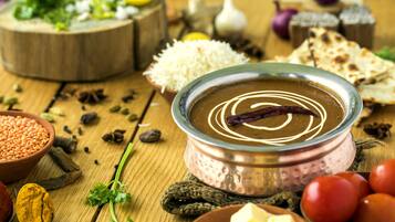 Comida tradicional india con un cuenco metálico de dal, rodeado de ingredientes como tomates, cebollas y especias.