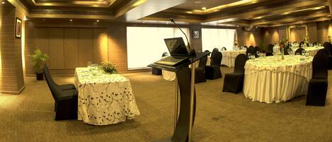 A conference room with round tables, chairs, and a podium with a laptop.