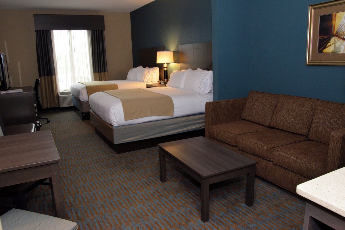 A hotel room with two beds, a sofa, a desk, and a TV.