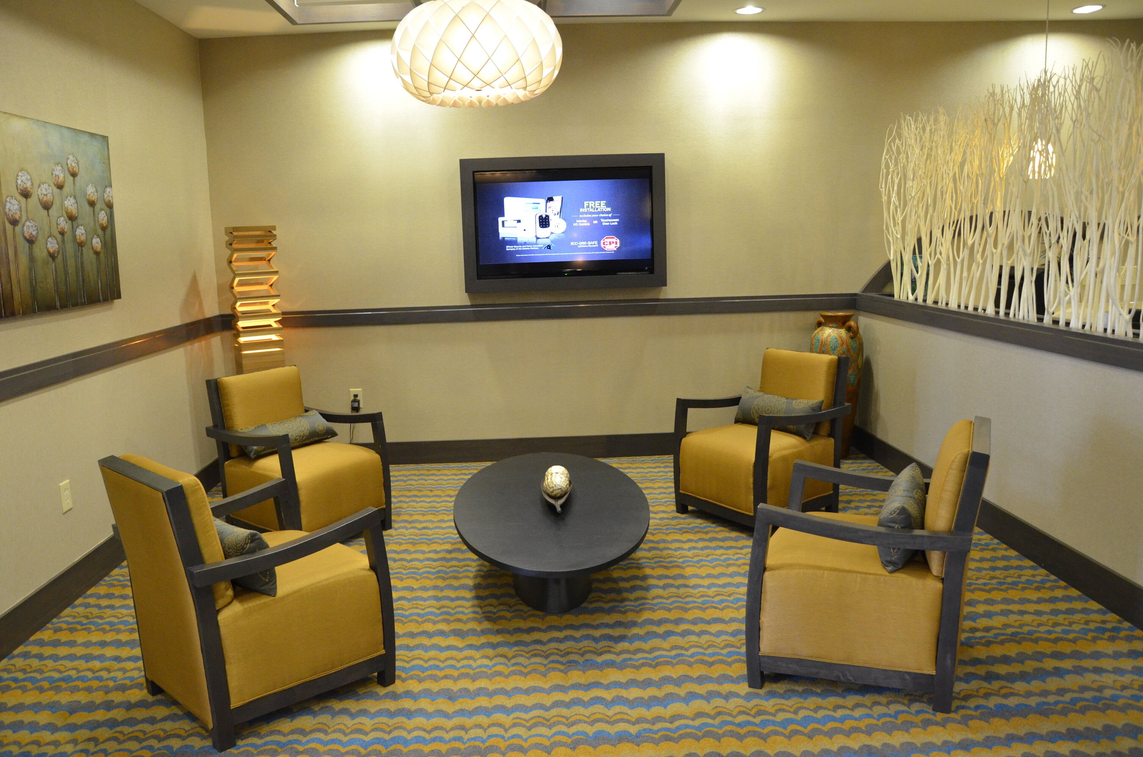 Ein Hotelzimmer mit einem an der Wand befestigten Fernseher, einem runden Couchtisch und vier Stühlen, die darum herum angeordnet sind.