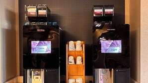 A coffee station with two espresso machines, a display of Costa Coffee branded products, and a wooden shelf with disposable cups. - Holiday Inn Express Hotel & Suites Goldsboro - Base Area by IHG (Goldsboro)