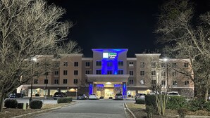 A Holiday Inn Express & Suites building with a central entrance, multiple parking spaces, and surrounding trees. - Holiday Inn Express Hotel & Suites Goldsboro - Base Area by IHG (Goldsboro)
