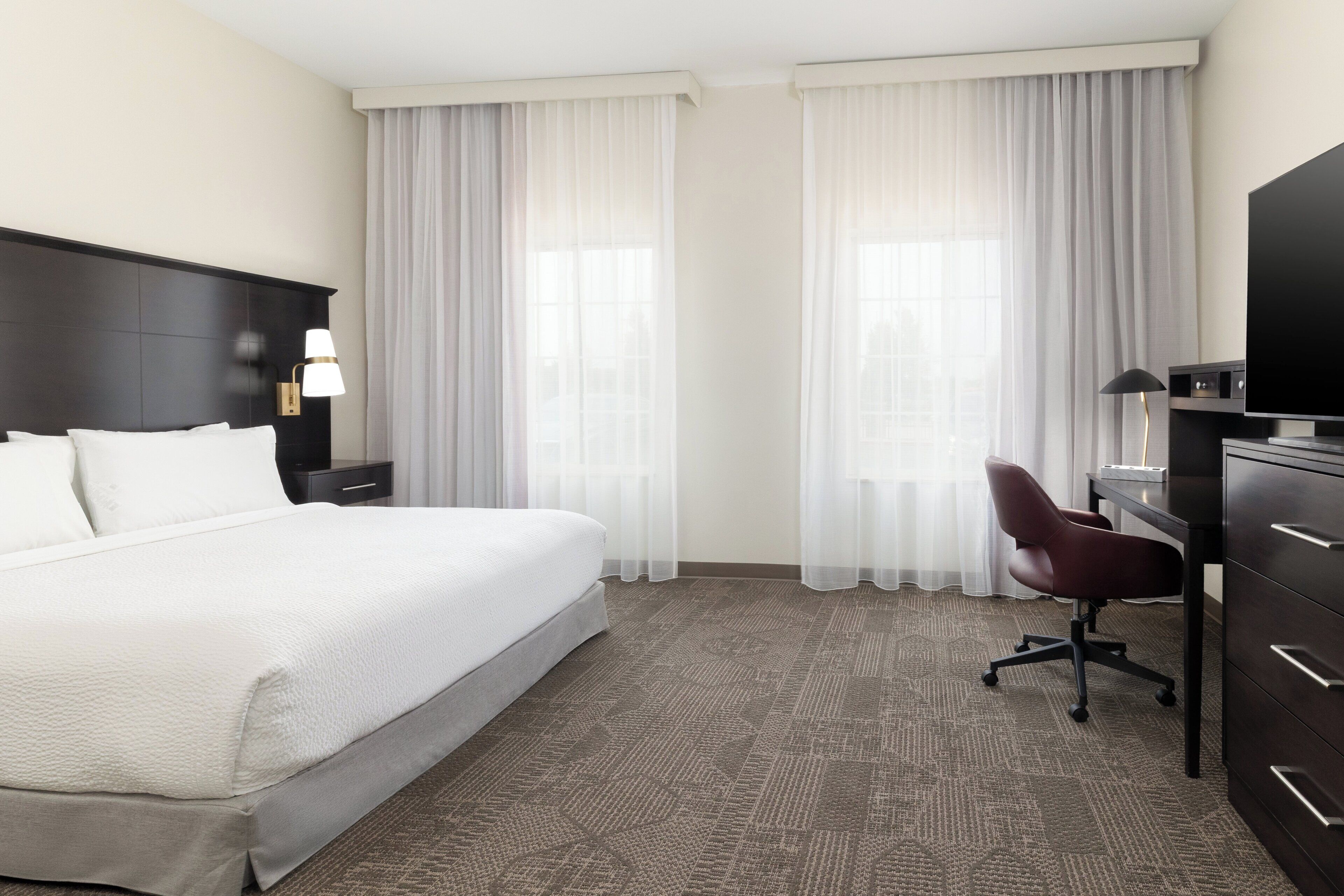 A hotel room with a large bed, a desk with a chair, a television, and a lamp.