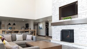 A modern living room with a sectional sofa, a flat-screen TV mounted above a fireplace, and a dining area in the background. - Staybridge Suites Denver-Central Park by IHG (Denver)