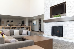 Una sala de estar moderna con un sofá modular, un televisor de pantalla plana sobre la chimenea y un comedor al fondo.