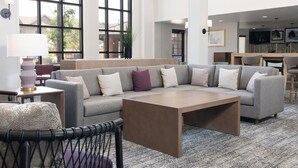 A modern living room with a sectional sofa, a coffee table, and a dining area with a kitchen in the background. - Staybridge Suites Denver-Central Park by IHG (Denver)