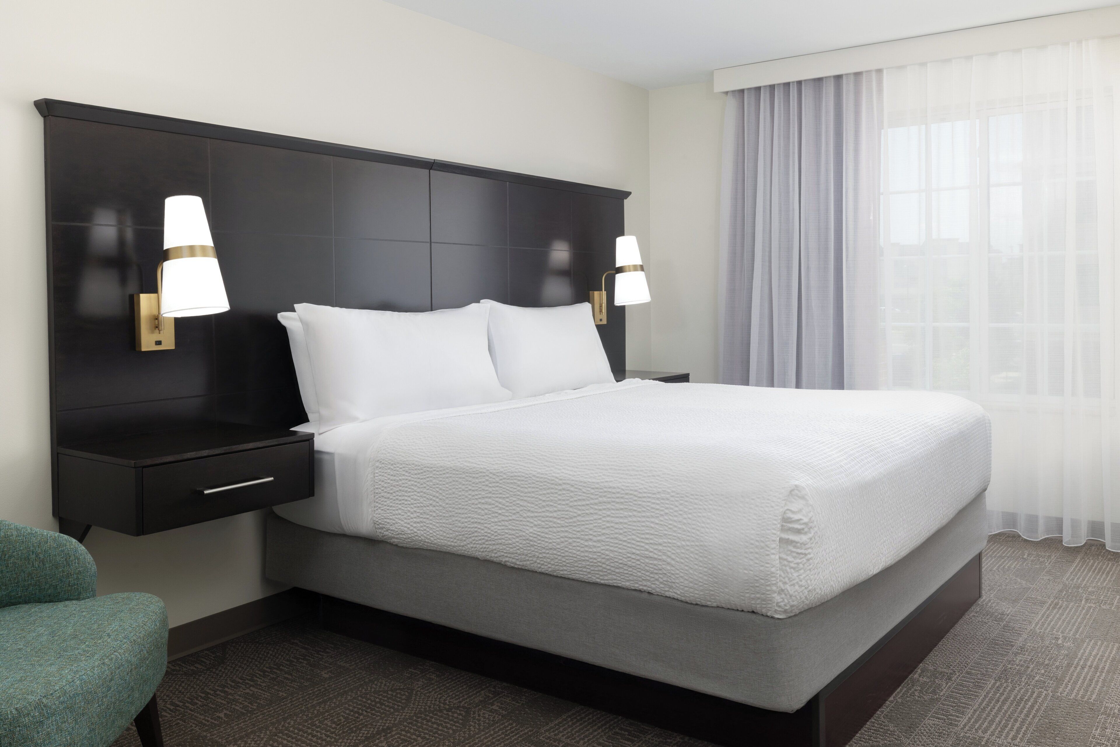 A hotel room with a large bed, two bedside tables with lamps, a nightstand, and a chair.