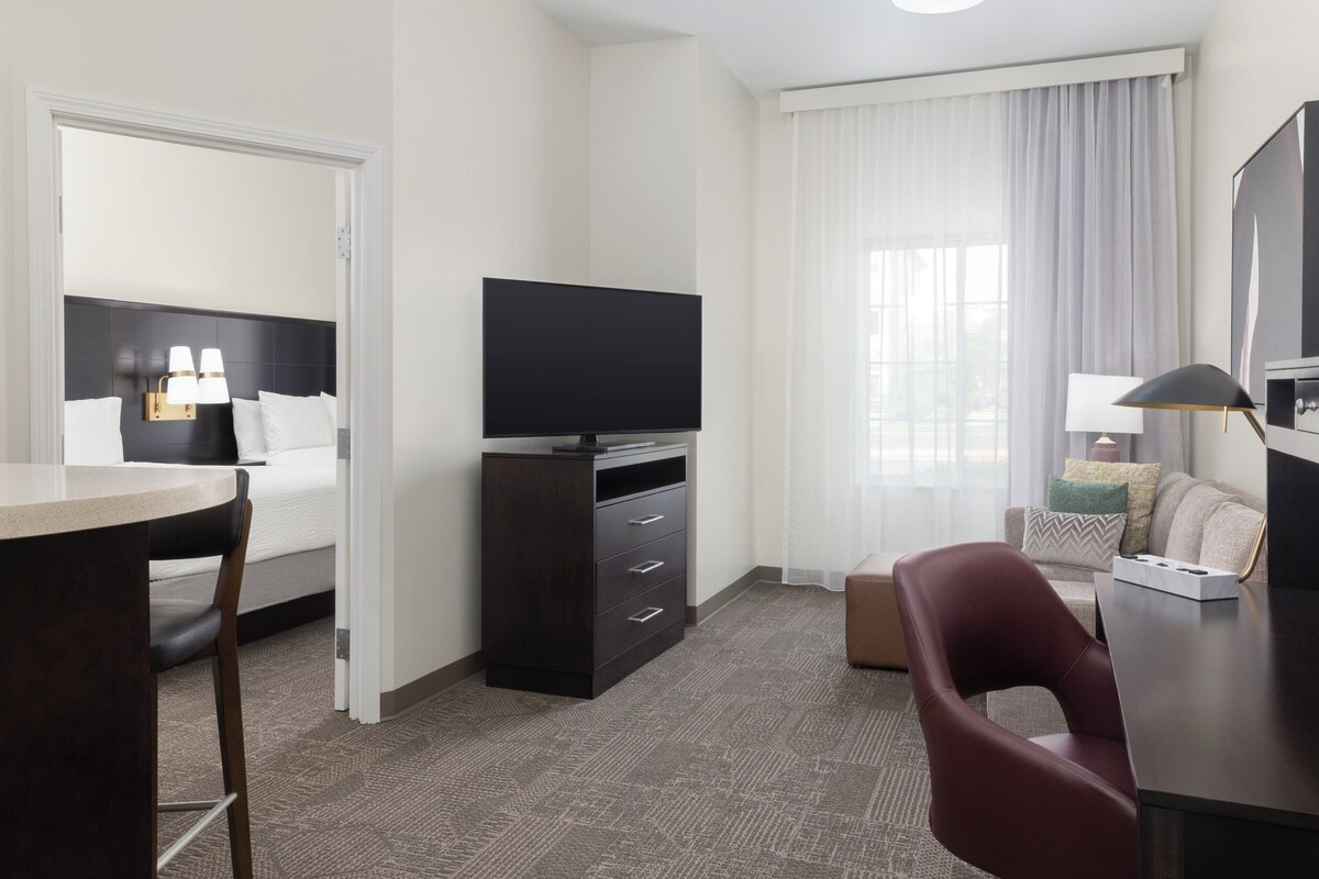A hotel room with a bed, a desk, a TV, a chair, and a window with curtains.