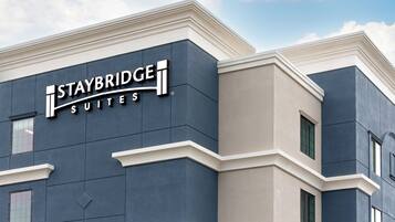 Un edificio Staybridge Suites con un diseño arquitectónico moderno, que presenta señalización destacada y una base de ladrillo.