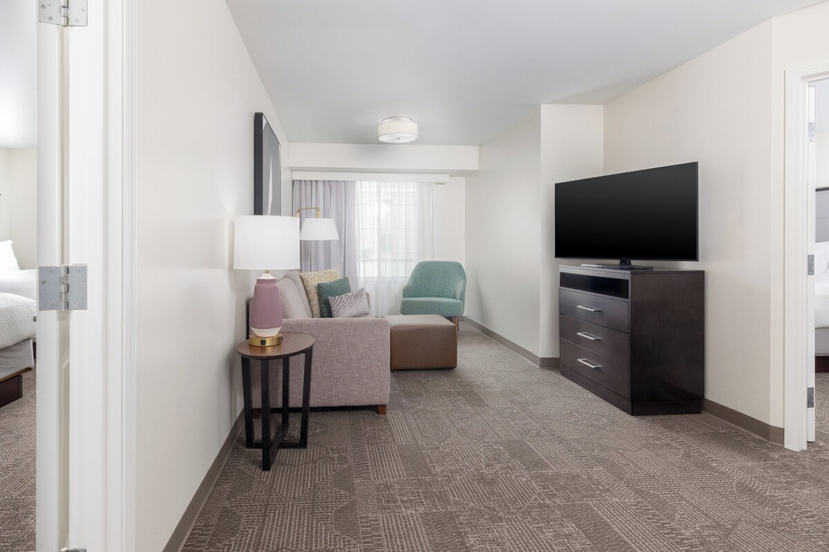 A hotel room with a bed, a sofa, a TV, a lamp, and a small table.