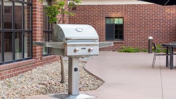 Una parrilla al aire libre sobre un soporte metálico, ubicada en un patio con un edificio de ladrillo al fondo.